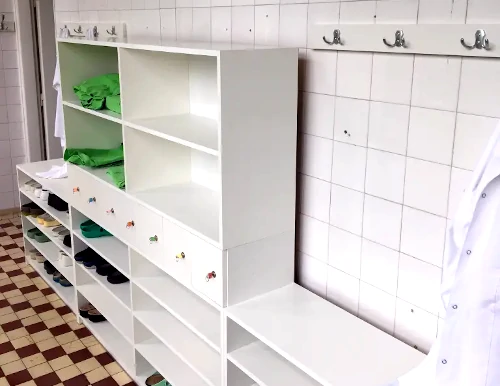 A képen egy fából készült, fehér korházi öltözőszekrény látszik cipőtárolóval, tuhatárolóval és zárható fiókokkal.